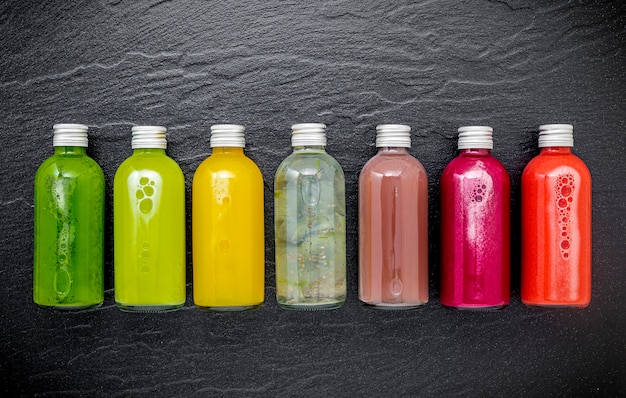 Smoothies saudáveis coloridos e sucos em garrafas no fundo escuro de pedra com espaço de cópia.