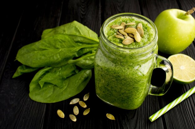 Smoothies verdes com sementes de espinafre, maçã e abóbora na mesa de madeira preta