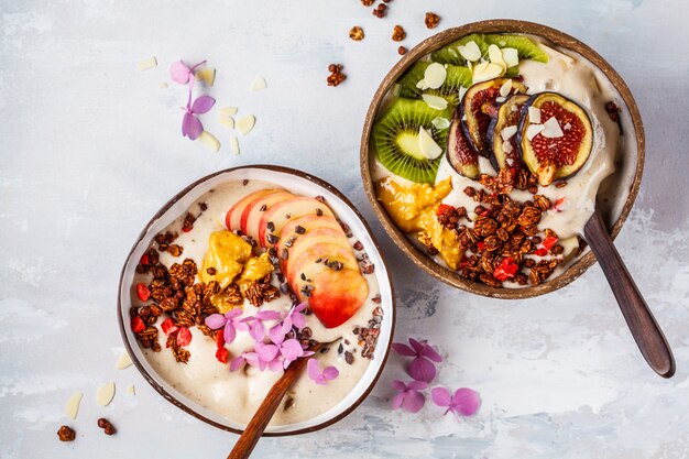 Smoothieschüssel mit Frucht und Granola mit Kokosschalenschüssel auf grauem Hintergrund. Gesundes veganes Essen.