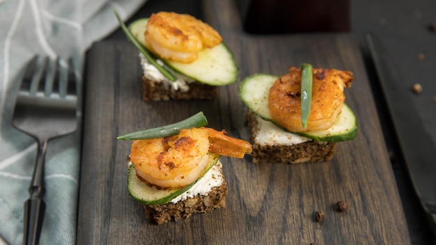 Smorrebrod de sándwich abierto danés con gambas, pepino y queso crema sobre tabla de servir de madera