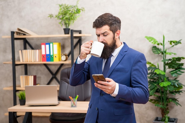 SMS para comunicação empresarial Chefe lendo mensagem no celular enquanto bebe café Mensagens SMS