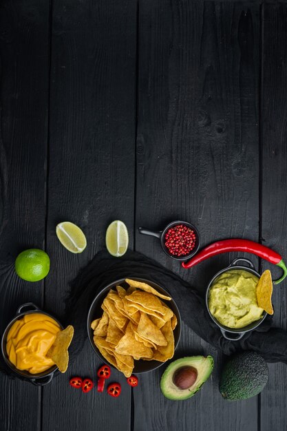 Snack crocante mexicano, chips de nachos e molho de abacate guacamole de queijo, em mesa de madeira preta, vista de cima ou plano plano