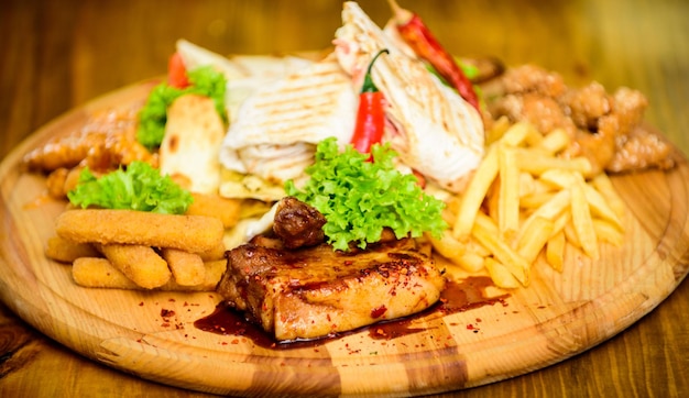 Snack für Bier. Holzbrett Pommes frites Fischstäbchen Burrito und Fleischsteak serviert mit Salat. Kneipenmenü-Snack. Guten Appetit. Fleischsnack für Gruppenfreunde. Leckere leckere Snacks. Essen im Restaurant.