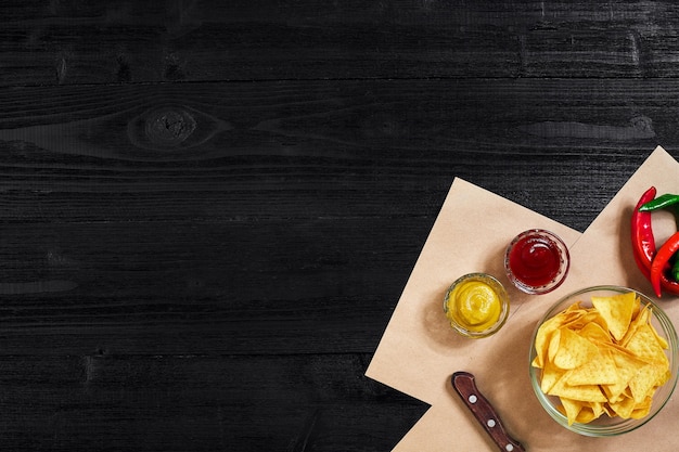 Snack für Partychips Nachos mit Saucen Tomatenketchup Senf auf einem schwarzen Hintergrund Draufsicht Kopie...