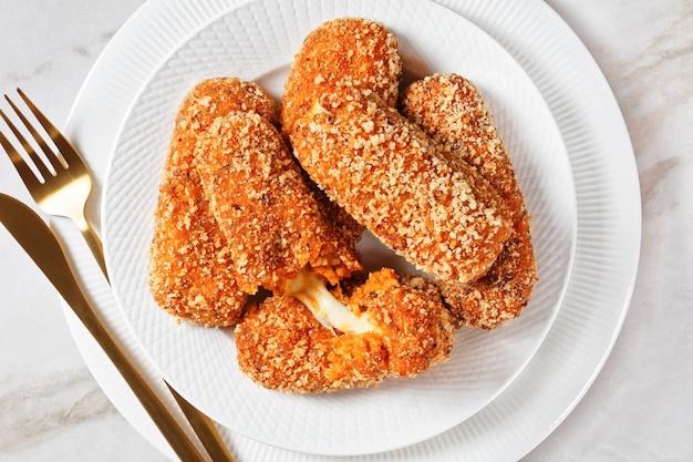 Snack italiano suppli al telefono o croquetas de arroz rellenas de queso mozzarella servido en un plato blanco sobre un fondo de mármol claro, vista superior, primer plano