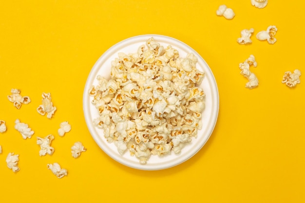Snack-Konzept Süßes Popcorn in weißer Platte und fällt auf gelben Hintergrund