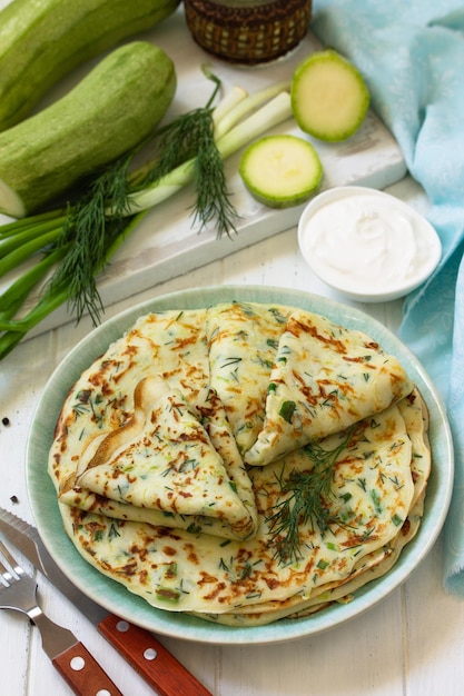 Snack oder Sommermittagessen Zucchini-Pfannkuchen mit Gemüse, serviert mit Sauerrahm auf einem Holztisch