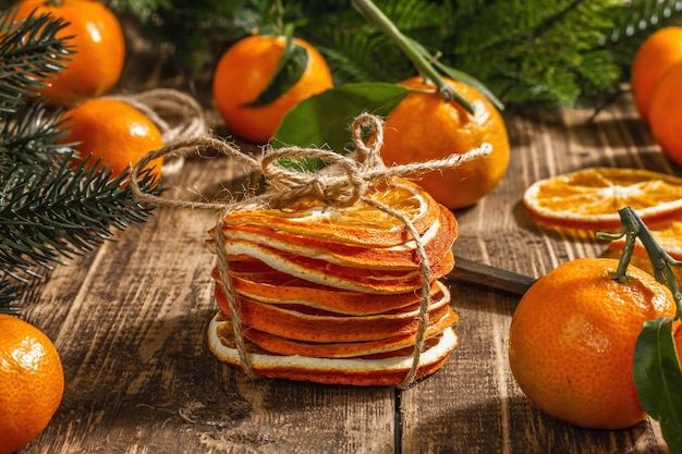 Snack de rodajas de naranjas secas. Cítricos secos para decoración navideña. Mandarinas con hojas, ramas de abeto, tijeras e hilo. Fondo de madera, concepto rústico, cerrar