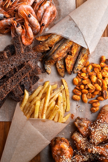 Snack zum Bier auf einem Holzbrett. Garnele. Gebratener Fisch. Gebratene Erdnüsse. Pommes. Hühnerflügel. Knirschen. Croutons.