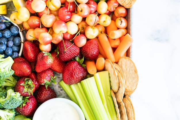 Snackboard mit frischem Obst, Gemüse, Crackern und Dips.