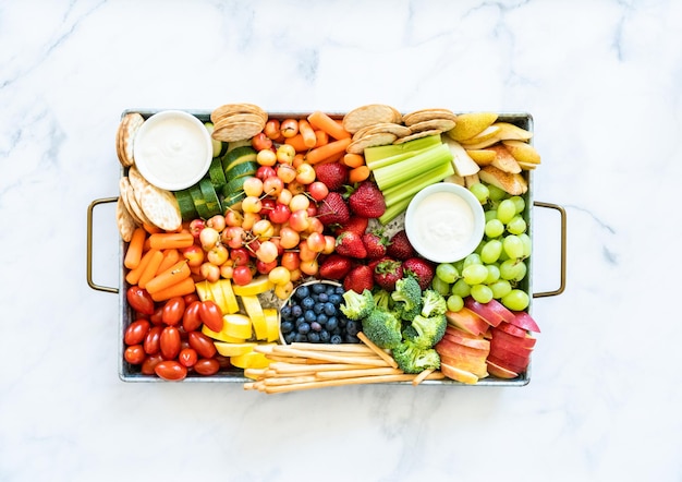 Snackbrett mit frischem Obst, Gemüse, Crackern und Dips.