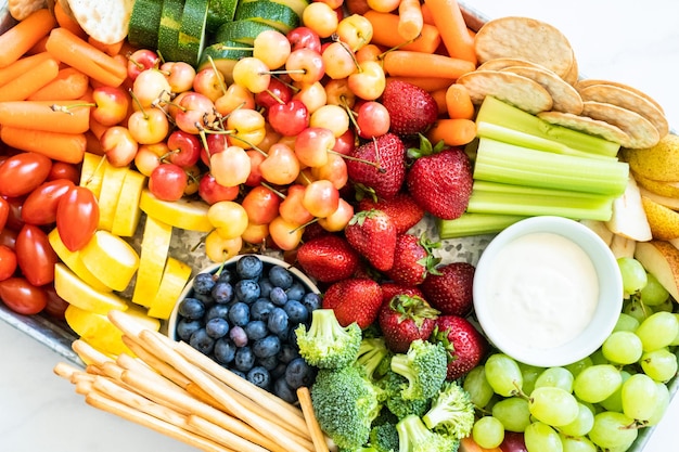 Snackbrett mit frischem Obst, Gemüse, Crackern und Dips.