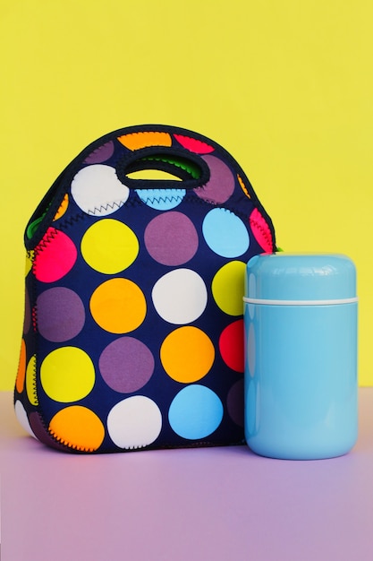 Snacken Sie eine Pause mit einer Lunchbox. bunte Handtasche, blaue Thermoskanne. Mittagessen für einen Schüler oder einen Büroangestellten. Platz für Text