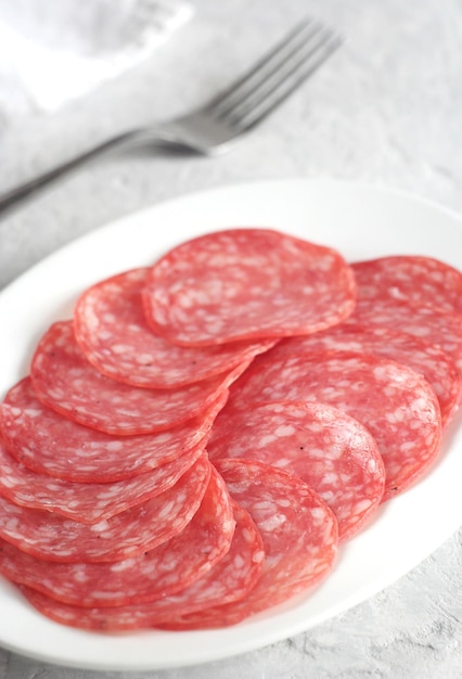 Snackteller mit Salamiwurst. Der Teller steht auf einem grauen Betontisch. Dahinter liegt ein Handtuch und eine Gabel