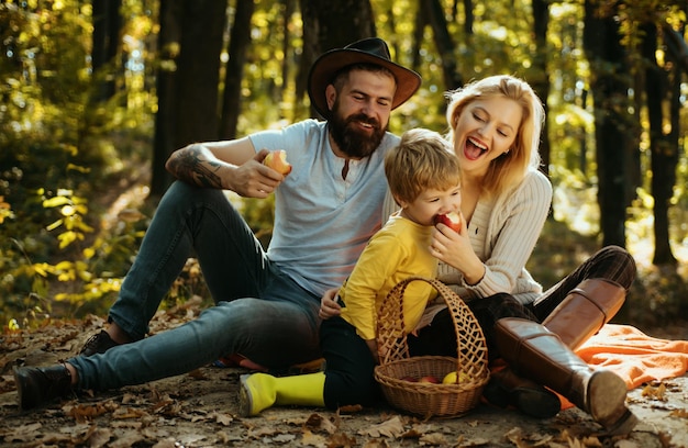 Snackzeit, glückliche Familie mit kleinem Jungen, der sich beim Wandern im Waldkorb entspannt