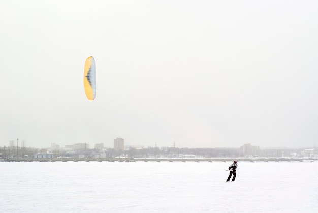 Snow kiter cabalga sobre el hielo de un lago congelado con el telón de fondo de la ciudad durante una nevada