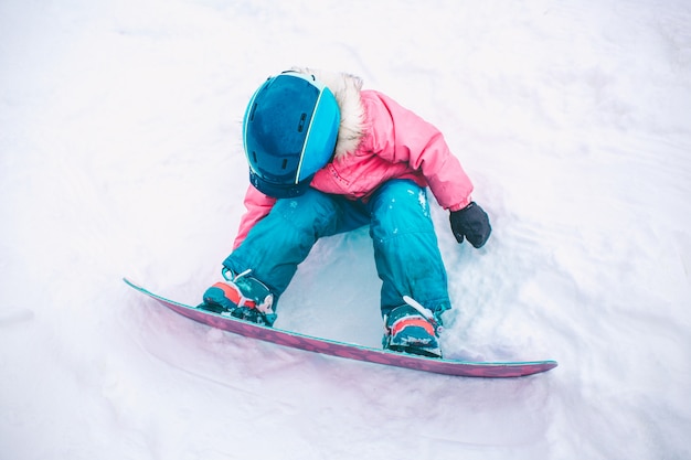 Snowboard Wintersport. Das Kleinkindmädchen, das mit dem Schnee trägt warme Winterkleidung spielt. Winter