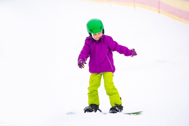 Snowboard-Wintersport. kleines Mädchen, das Snowboarden lernt und warme Winterkleidung trägt. Winter-Hintergrund.