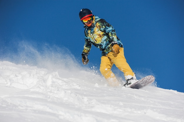 Snowboarder activo en ropa deportiva brillante bajando por una ladera de montaña en polvo