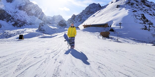 Snowboarder camina cuesta abajo con una tabla de snowboard en la mano.