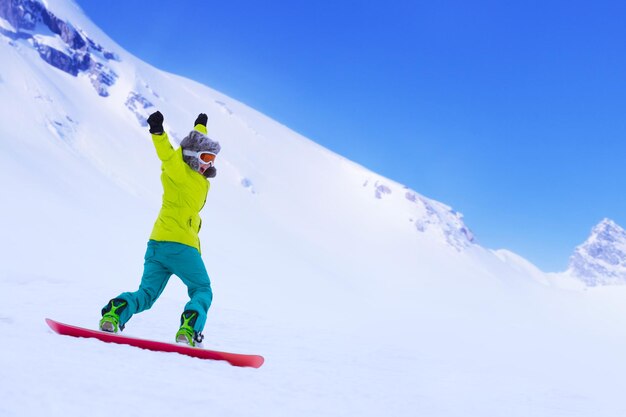 Snowboarder chica corriendo por la ladera en las montañas alpinas. Deportes de invierno y recreación, actividades de ocio al aire libre. Imagen del concepto de disfrute de mujer joven gritando emocionado