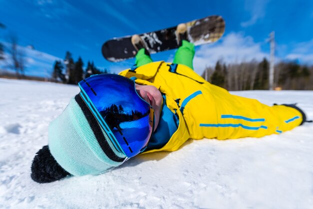 Snowboarder deitado de costas em um dia ensolarado.