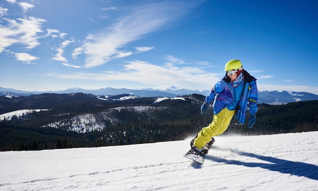 Snowboarder, der an einem sonnigen Wintertag mit dem Snowboard den schneebedeckten Berghang hinunterfährt Extremsportkonzept