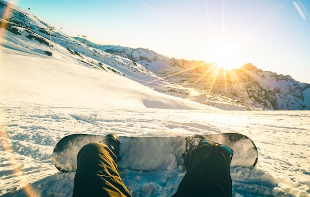 Snowboarder, der bei Sonnenuntergang im Entspannungsmoment im Skigebiet der französischen Alpen sitzt