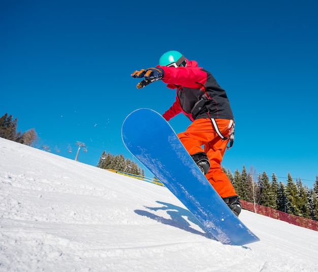 Snowboarder, der in der Luft springt, während er auf der Piste im Winterskigebiet in den Bergen reitet