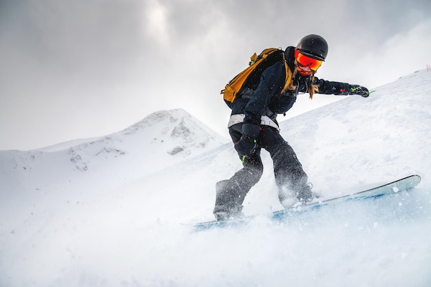 El snowboarder desciende rápidamente creando una ola de nieve con el telón de fondo de las montañas de la estación de esquí