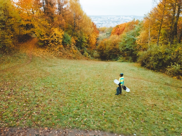 Snowboarder esperando la temporada de esquí de pie en pendiente de otoño