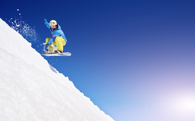 Foto snowboarder free rider saltando en el aire cuesta abajo en el fondo del espacio de copia de cielo azul y nieve blanca