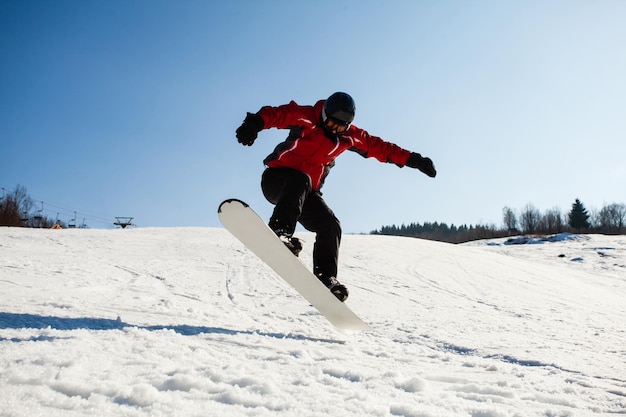 Snowboarder habilidoso pulando sobre a encosta de neve Colina de dia ensolarado de inverno coberta de neve snowboarder masculino em ação