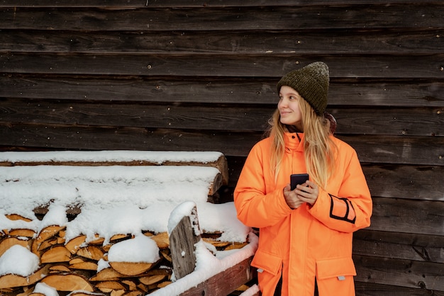 Foto snowboarder hermosa chica de pie solo con el teléfono en las manos. montaña al aire libre, actividad deportiva de invierno.