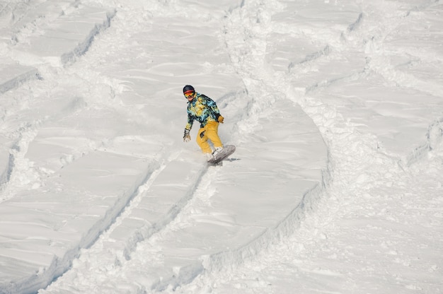 Snowboarder in heller Sportbekleidung, der an hellem Wintertag einen Schneehügel hinunter reitet