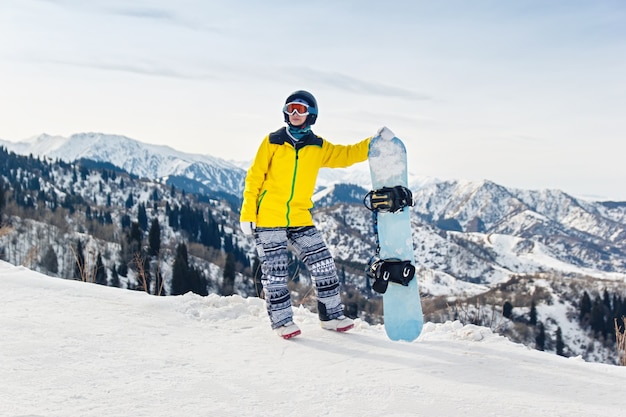 Snowboarder joven en una chaqueta amarilla y casco negro en el fondo de montañas nevadas