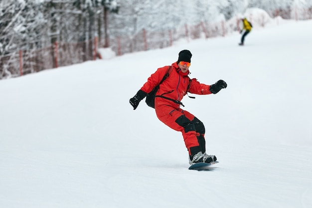 Snowboarder masculino com um terno vermelho cavalga na colina de neve com o conceito de snowboard, esqui e snowboard