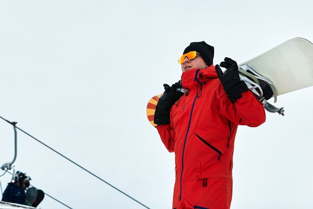Snowboarder masculino em um terno vermelho caminhando na colina de neve com conceito de snowboard, esqui e snowboard