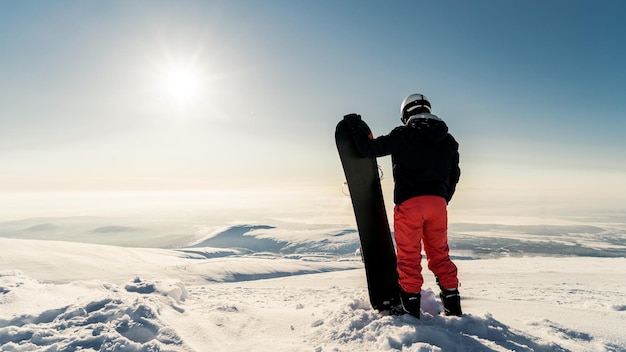 Un snowboarder masculino con equipo de snowboard en la cima de una montaña con vistas al pico del horizonte