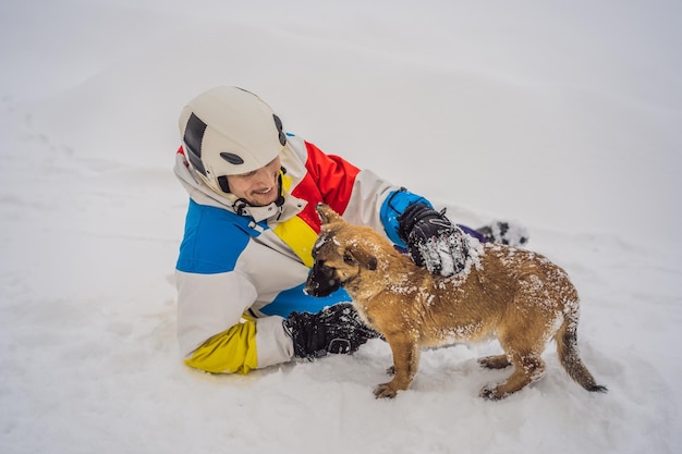 Snowboarder masculino jovem brinca com cachorros em uma estação de esqui no inverno