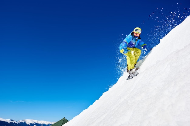 Snowboarder montando snowboard na encosta da montanha nevada no dia ensolarado de inverno Conceito de esporte radical