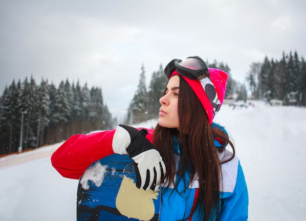 Snowboarder de mujer en invierno en la estación de esquí en el fondo de pinos