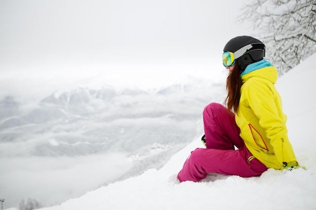 Foto snowboarder mujer sentada en la ladera de la montaña de nieve