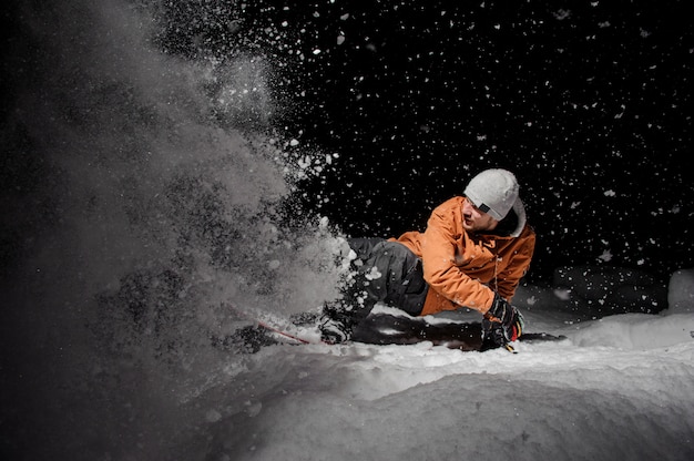 Snowboarder na jaqueta laranja, montando em uma colina de neve à noite