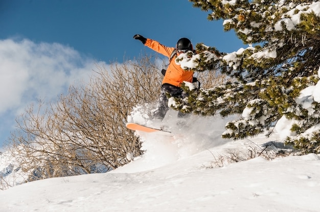 Snowboarder no sportswear laranja pulando na encosta da montanha em pó