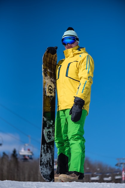 Snowboarder de pie con su tabla de snowboard en un día soleado