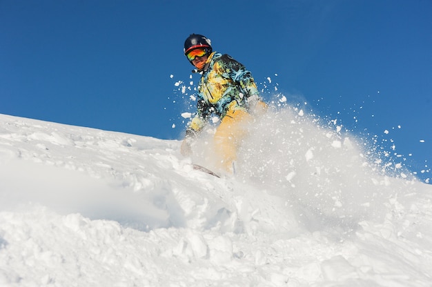 Snowboarder profesional activo en ropa deportiva brillante bajando por una ladera de montaña en polvo