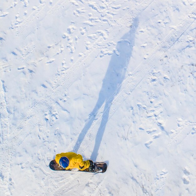 Snowboarder en ropa amarilla con sombra en vista aérea amarilla