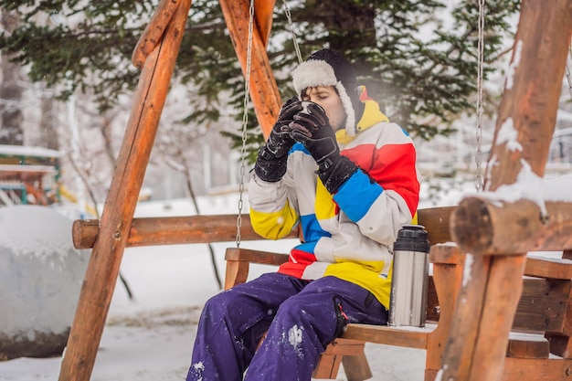 Snowboarder trinkt Tee aus einer Thermoskanne in einem Skigebiet