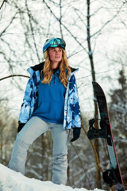 Snowboarderin im hellen Anzug in einer Sportbrille hält ein Snowboard. Extremsportarten. Freizeit.